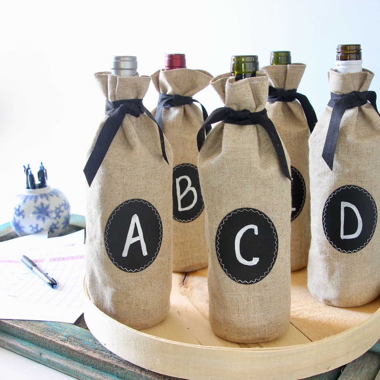 Five wine bottles in lettered bags on a cheese box lid