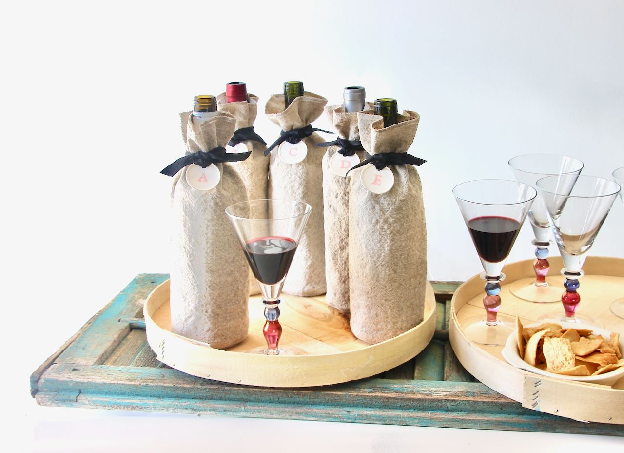Five bottle of wine hidden in washed linen bags with lettered tags around the necks ready for a blind wine tasting party