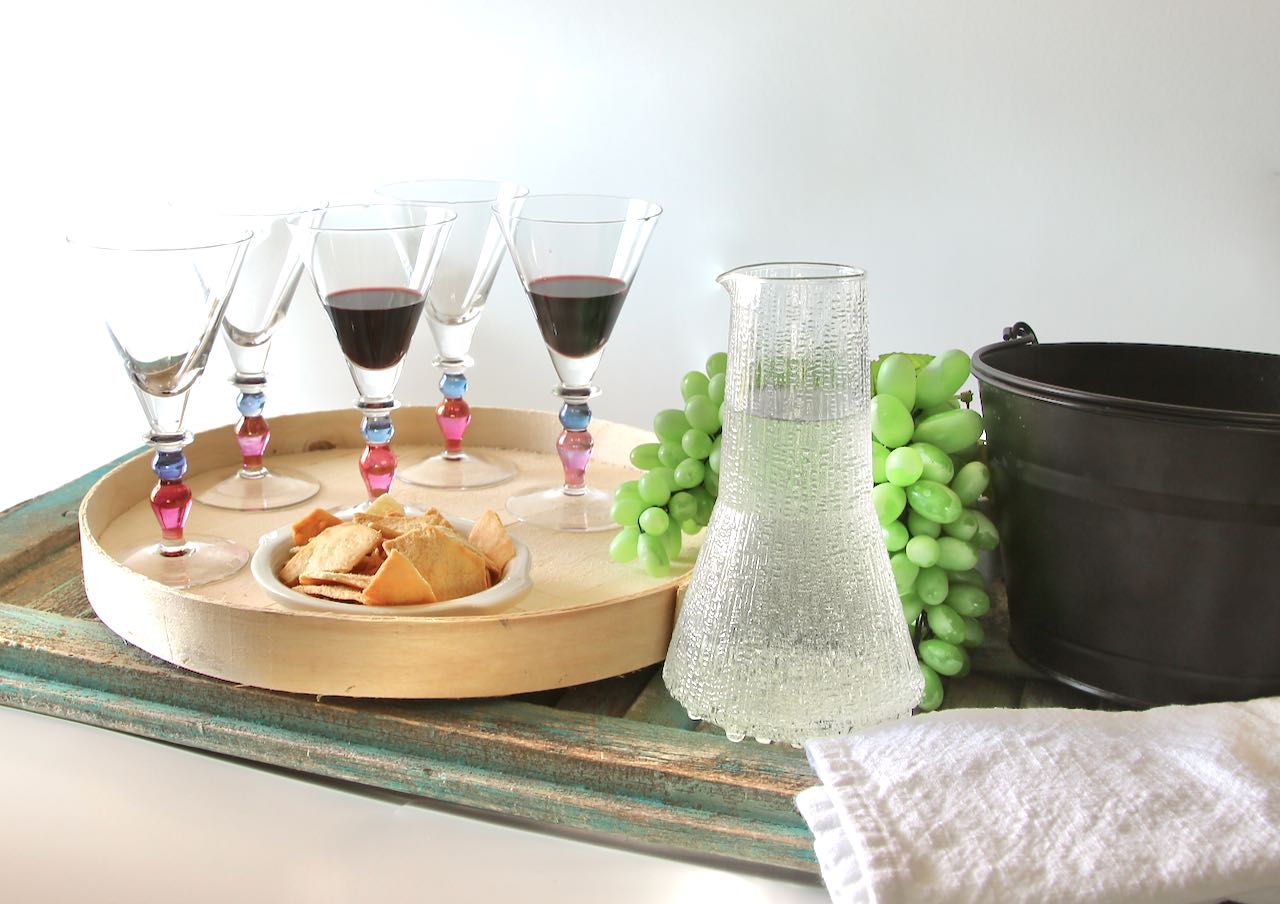 Glasses of wine on a treay with a pitcher of water and a large basin and a dish towel for cleaning the glasses between the blind wine tastings