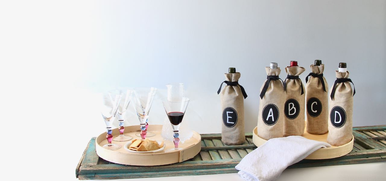 Blind Wine Tasting Party set up of wine glasses on a tray and Five mystery bottles of wine in linen bags with chalk cloth labels