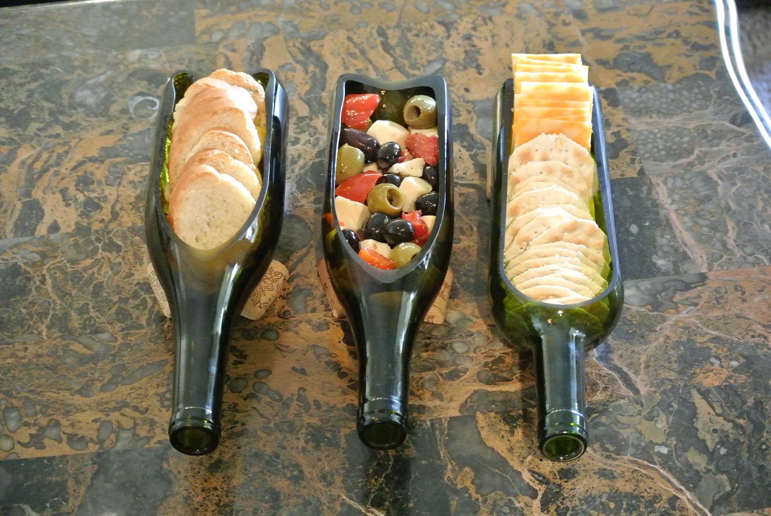 Three wine bottles cut in half lengthwise and laying down holding crackers or olives