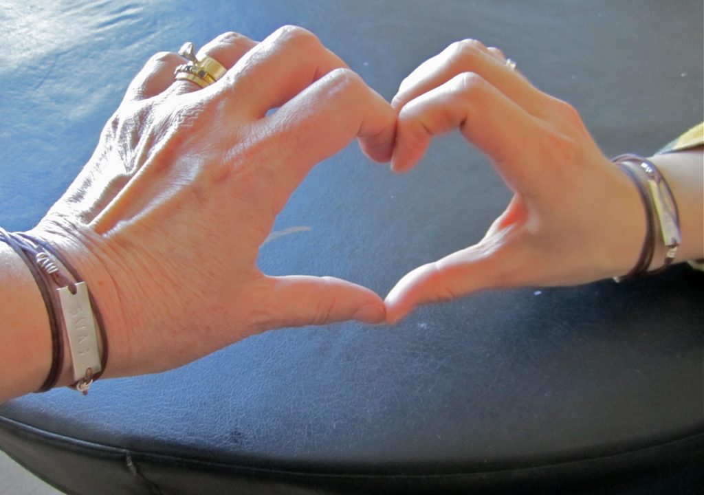 Mother & daughter's hand making s heart both wearing their SWAG bracelets.