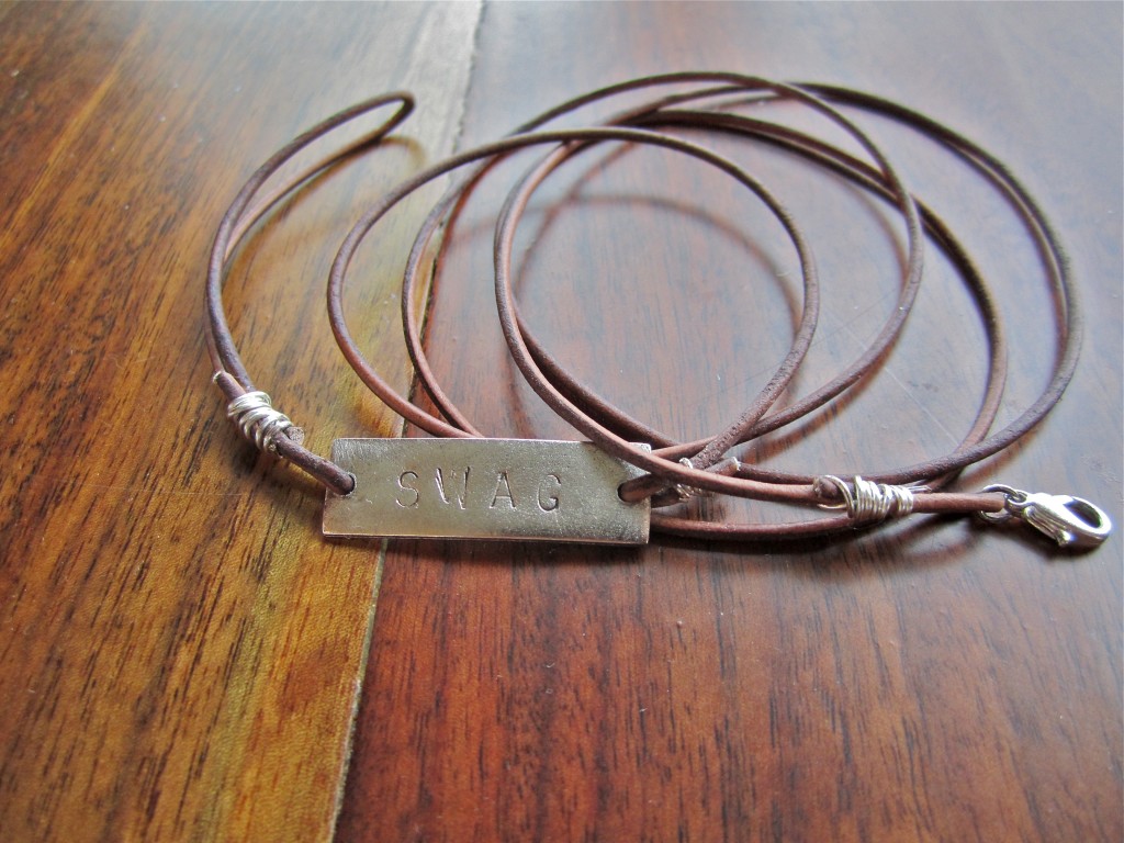 Leather strap with SWAG stamped metal tag bracelet on wood table.
