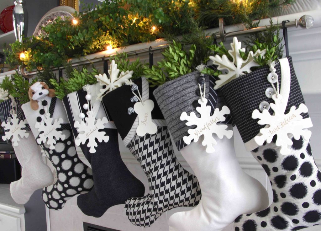 Black and white Christmas Stockings with snowflake name tags hanging from silver curtain rod.