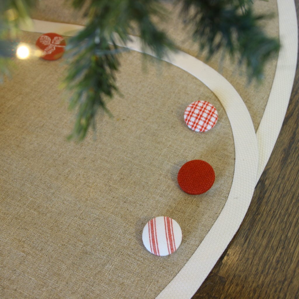 Closeup of linen tree skirt with creamy white trim and red and white buttons