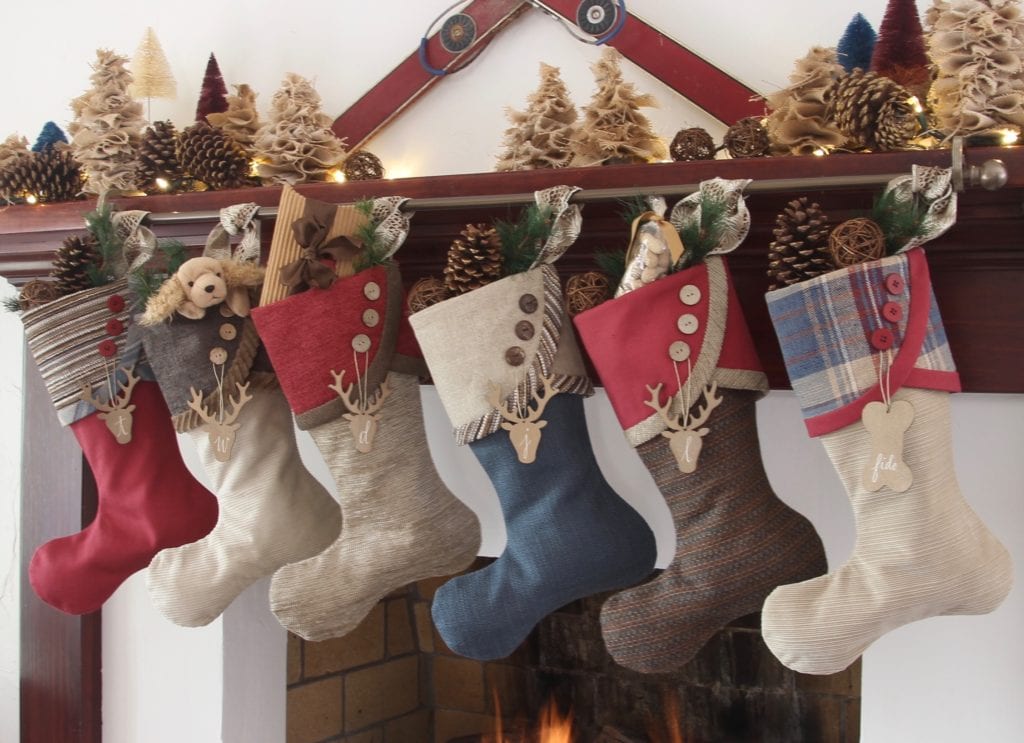 Set of 6 red, blue and tan Christmas stockings hanging on from mantel with vintage skis and burlap and bottle brush trees