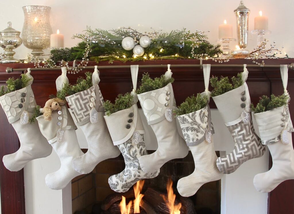 Set of eight silver and grey Christmas stockings hanging on mantel with mercury glass candles and beads and greenery 