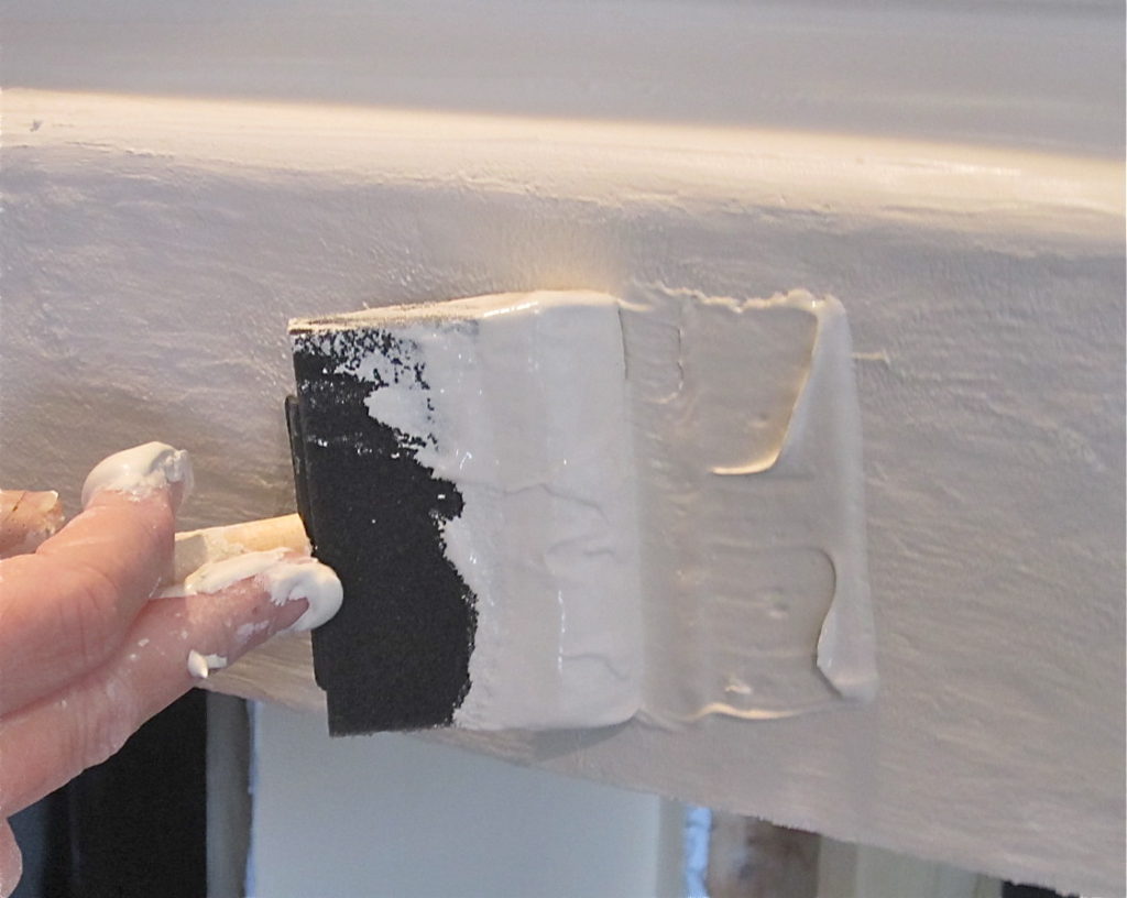 Using a wide foam brush to spread tinted joint compound onto the fireplace mantel