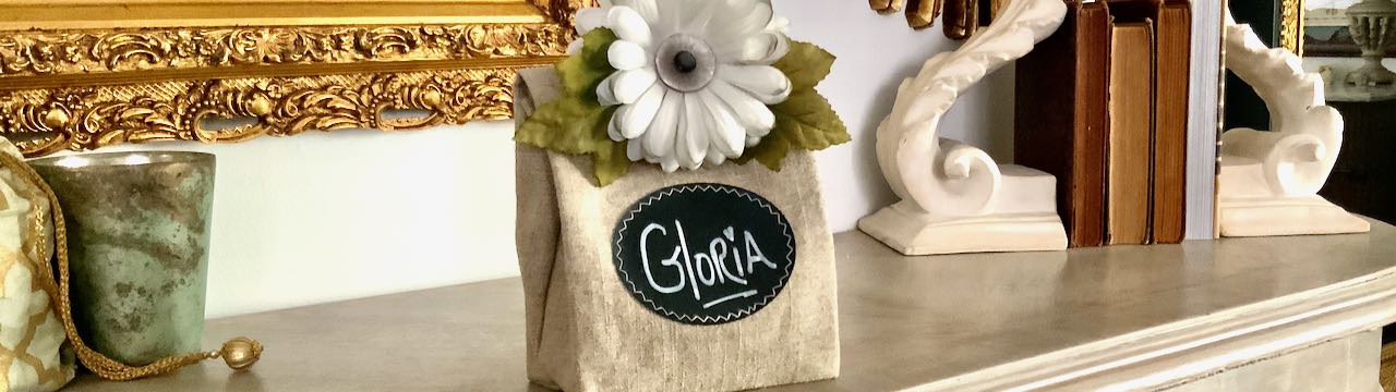 wide view of linen party bag "Gloria" with white mum closure on table with gold mirrors above and a row of antique books behind