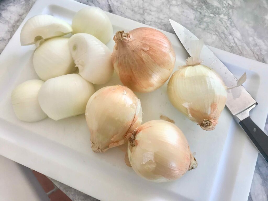 7 large onions on cutting board with chefs knife
