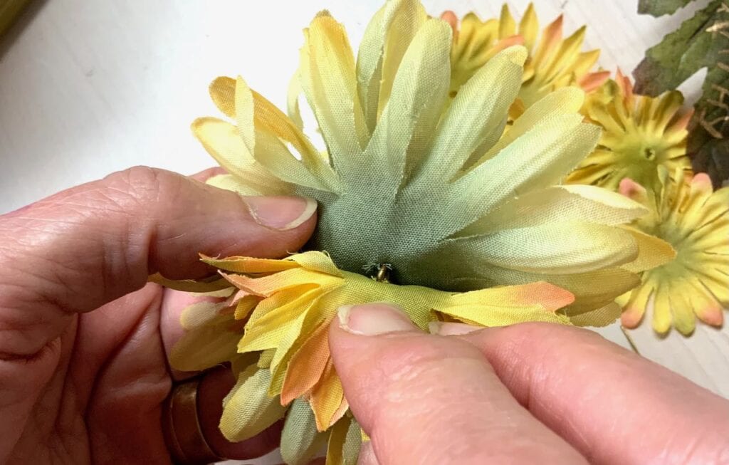 fingers pulling back layers of silk flower petals showing shank between them