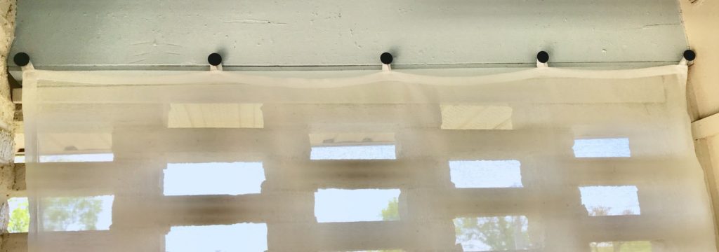 Closeup of black knobs holding sheer curtain panel tautly
