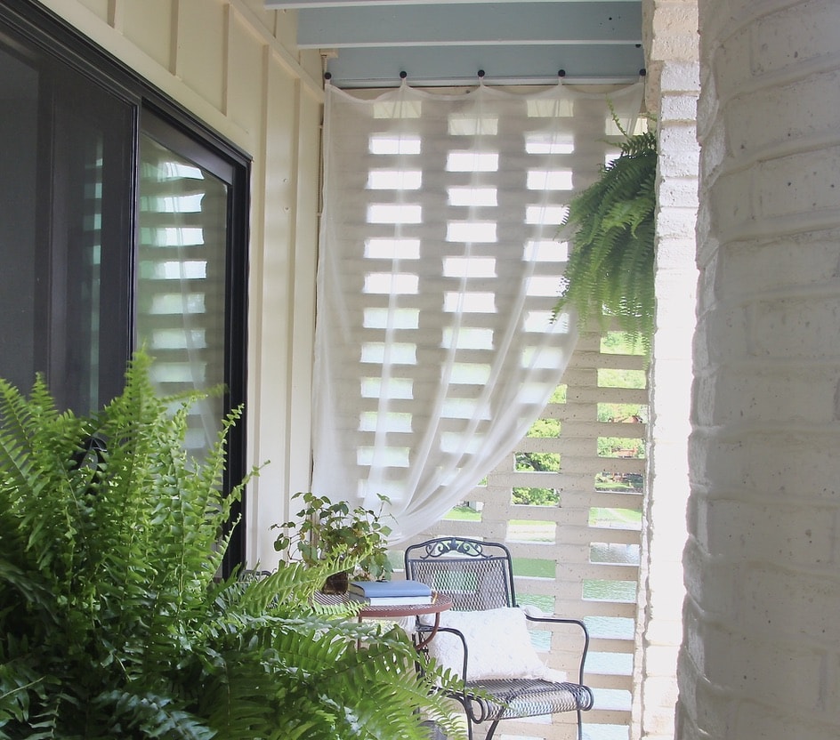 Sheer white curtain panel hanging outside with boston ferns
