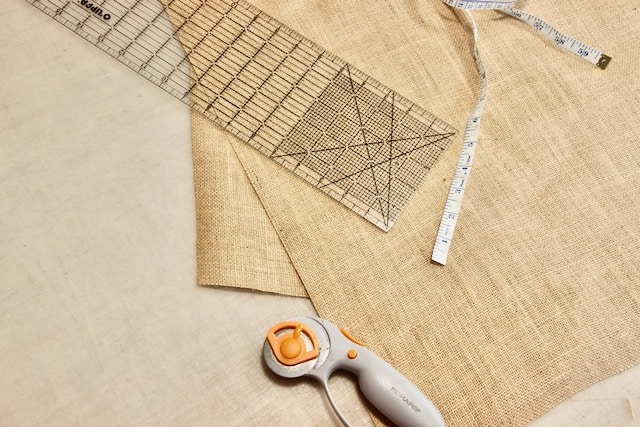 burlap, ruler, tape measure and rotary cutter on a cutting tablle