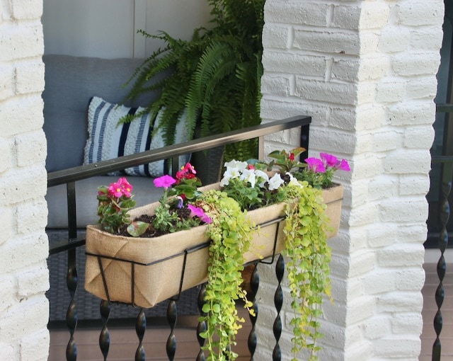 Burlap lined planter is full of bright summer flowers hanging on a balcony railing