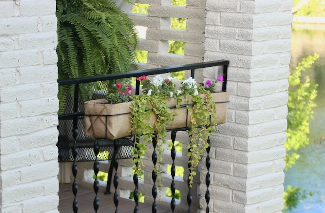 Iron blacony railing planter with burlap liner is planted with bright flowers and greens