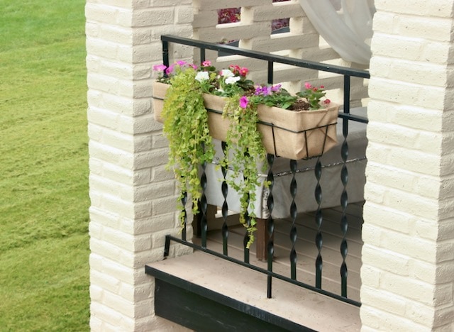 Iron planter with a burlap liner hhanging on a iron railing between brick columns
