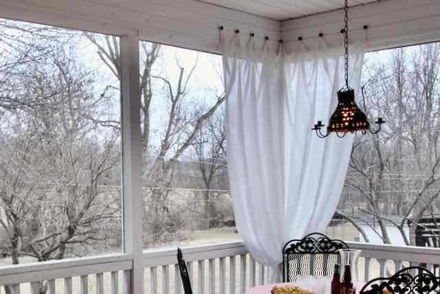 Sheer white curtain panels hanging on screened porch