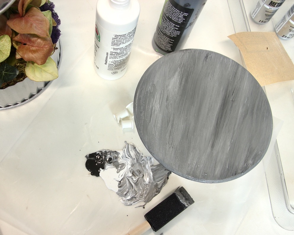 Base coat of striated gray paint on wooden disc.