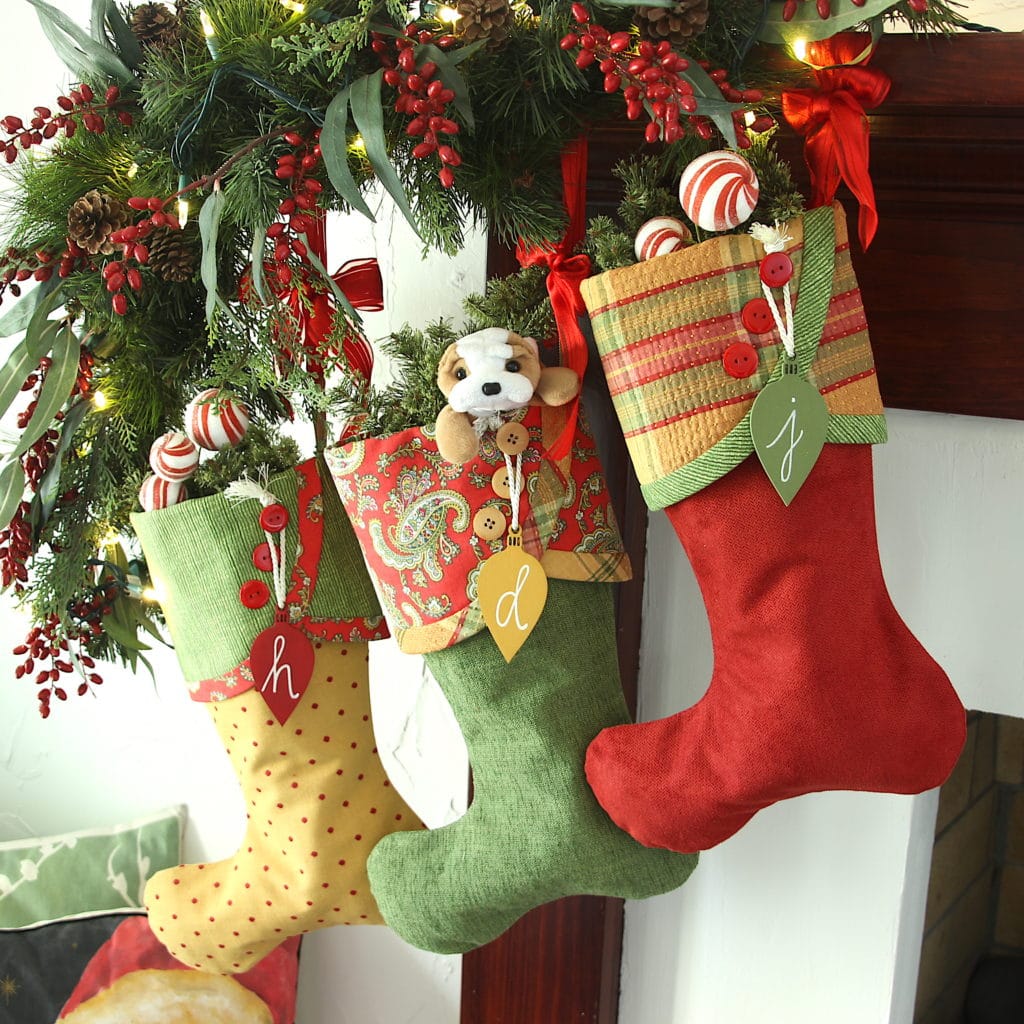 Three red, green and gold Christmas stocking hanging on a mantel