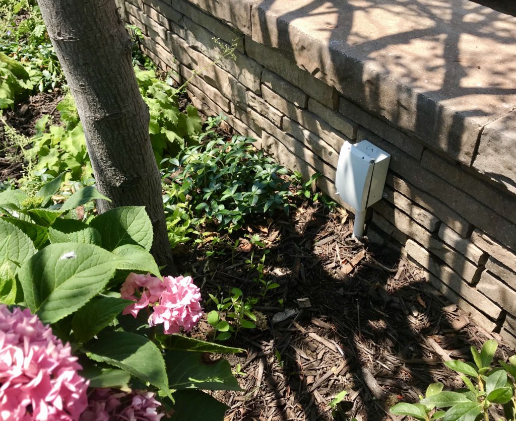 Before picture of white power box on pole against a stone landscaping knee wall.