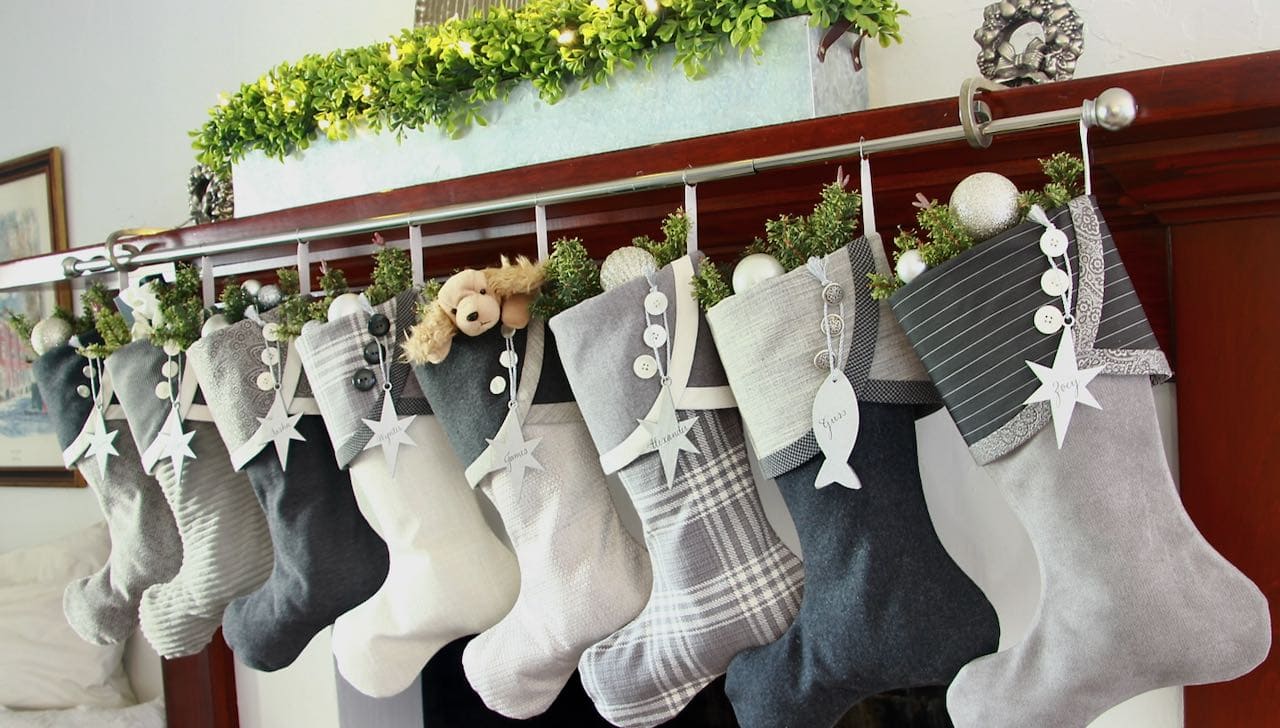 8 unique grey and white Christmas stockings hanging from a rod on the mantel with a boxwood planter for a modern minimalist Christmas display