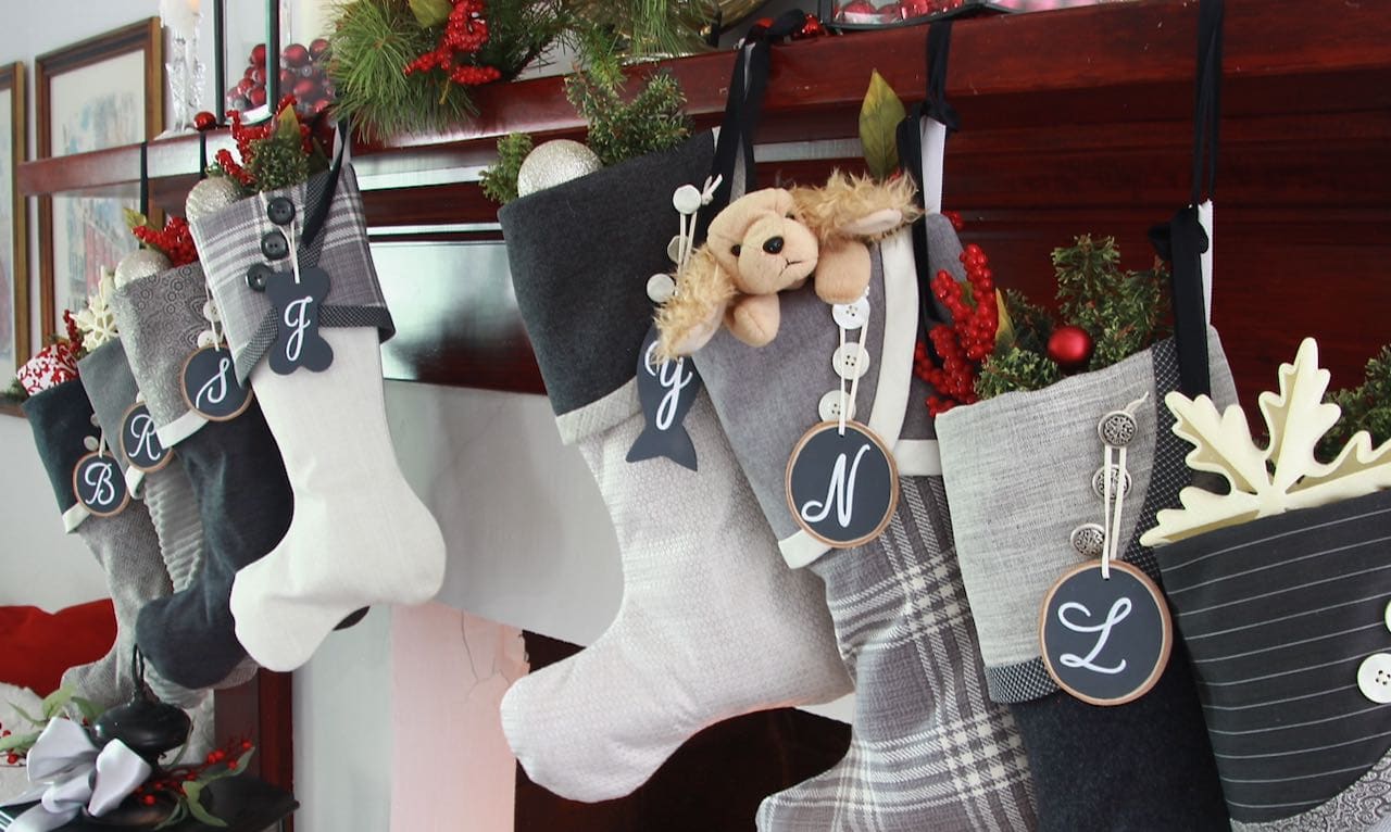 & out of 8 Grey Christmas stockings are displayed hanging individually at different height with large birch slice nametags with a single white initial
