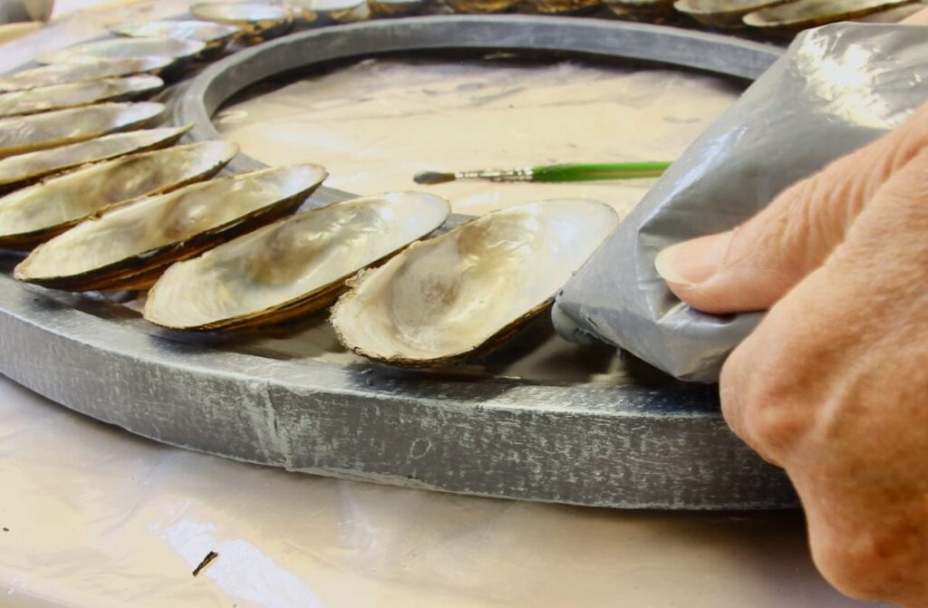 A freezer bag being squeezed to apply the tinted joint compound under and between the edges of the shells