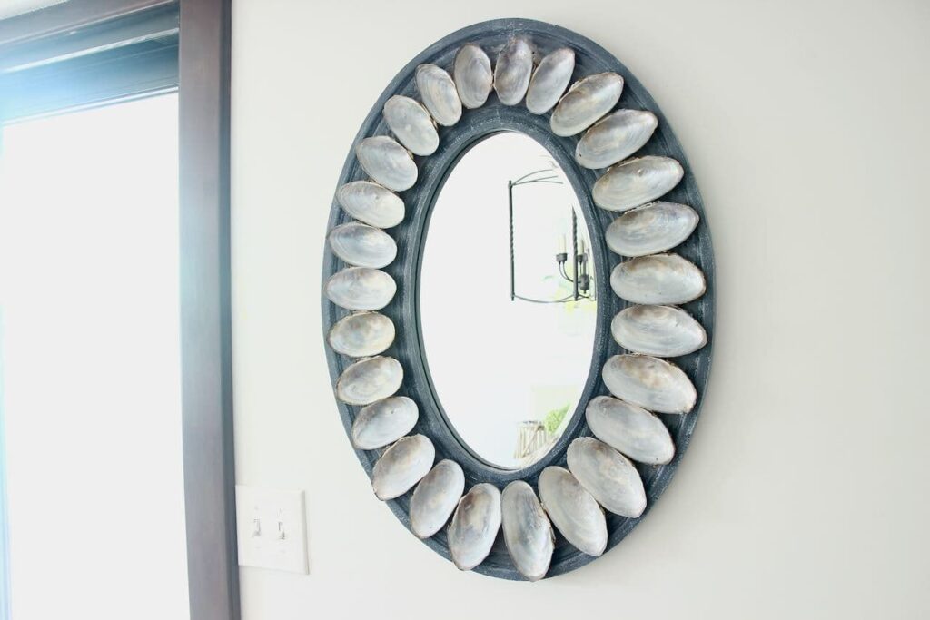 Shell mirror hanging on white wall reflecting a black iron light fixture