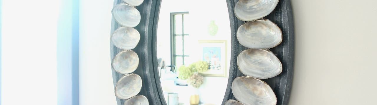 Cropped section of shell mirror hanging on a white wall with bright daylight streaming in on the left