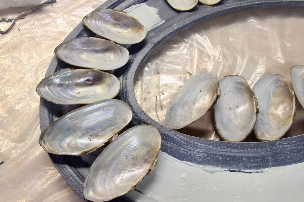 Shows a thick spread of tinted joint compound on the flat section of the frame and some of the shells waiting to be placed.