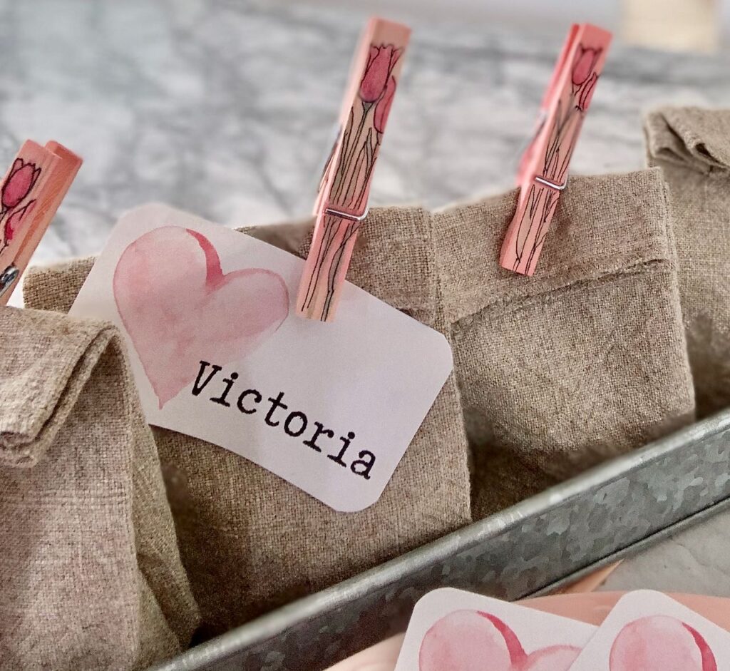 One name tag clipped on a washed linen party favor bag with additional bags in a galvanized metal tray on a quartz countertop