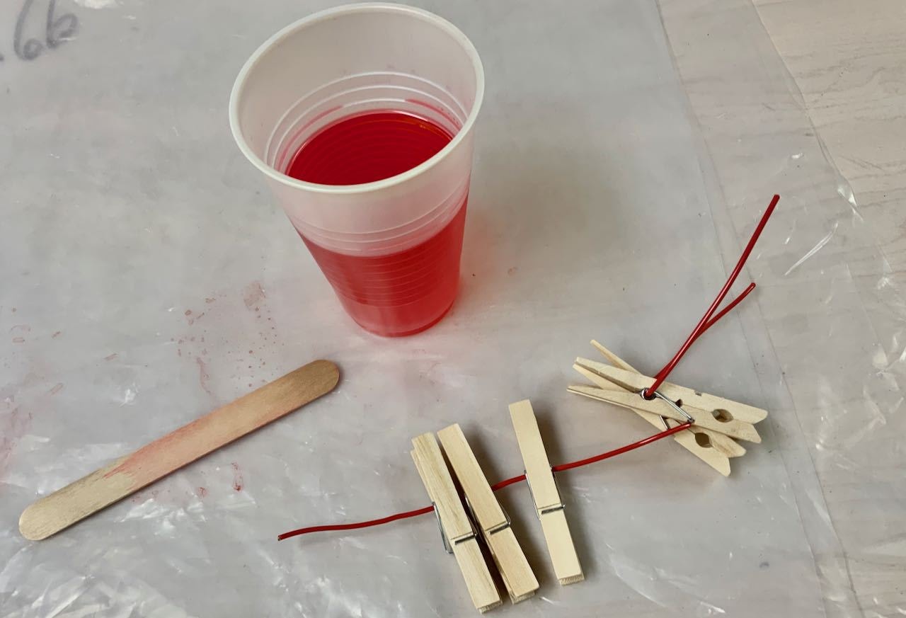 Cup of red dye with six clothespins strung on wire