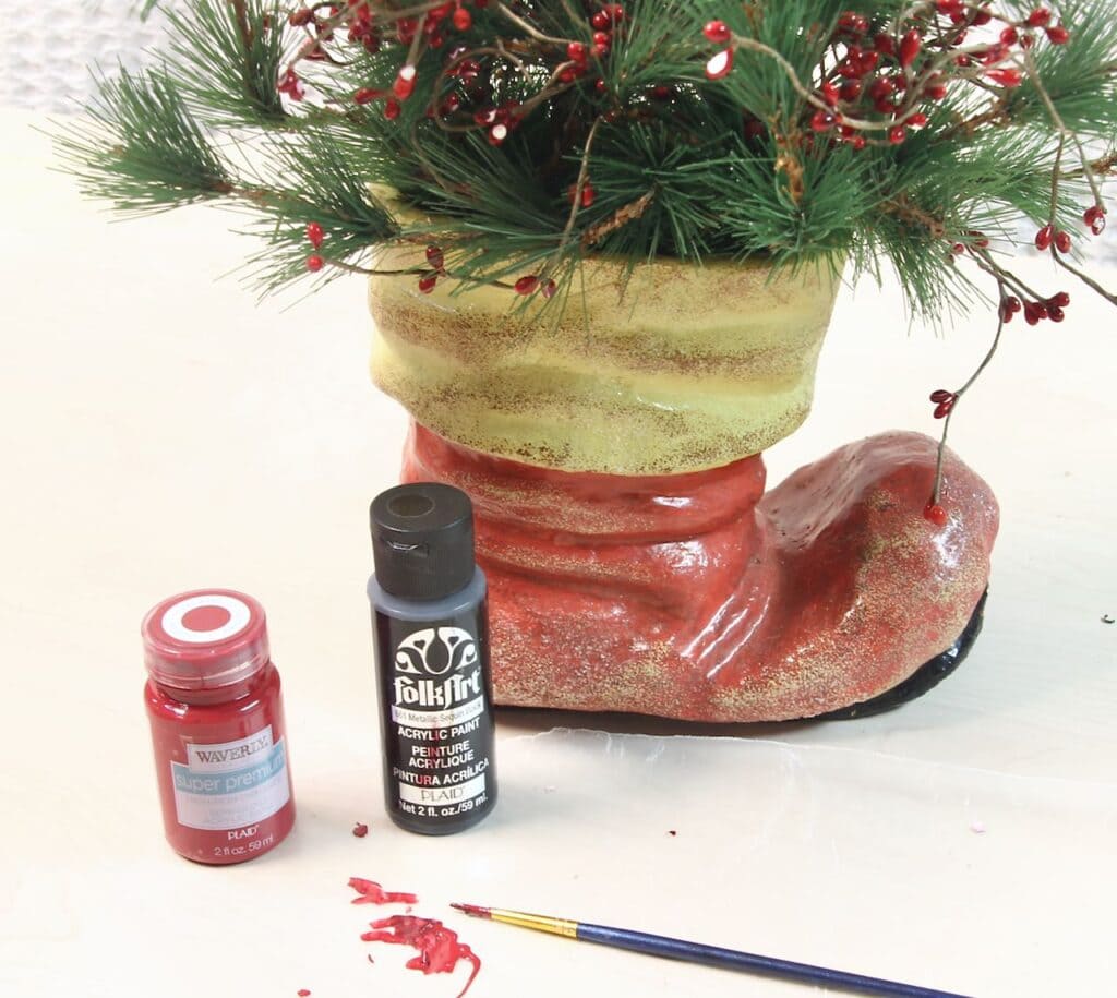 Red and black craft paint on wax paper with a brush by Santa's ceramic boot