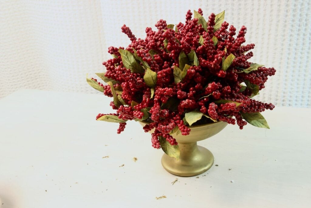 Gold footed basin filled with red berry stems and green leaves.