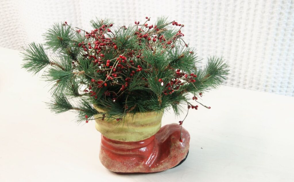 Ceramic Santa boot with pine boughs and berries coming overflowing from the cuff