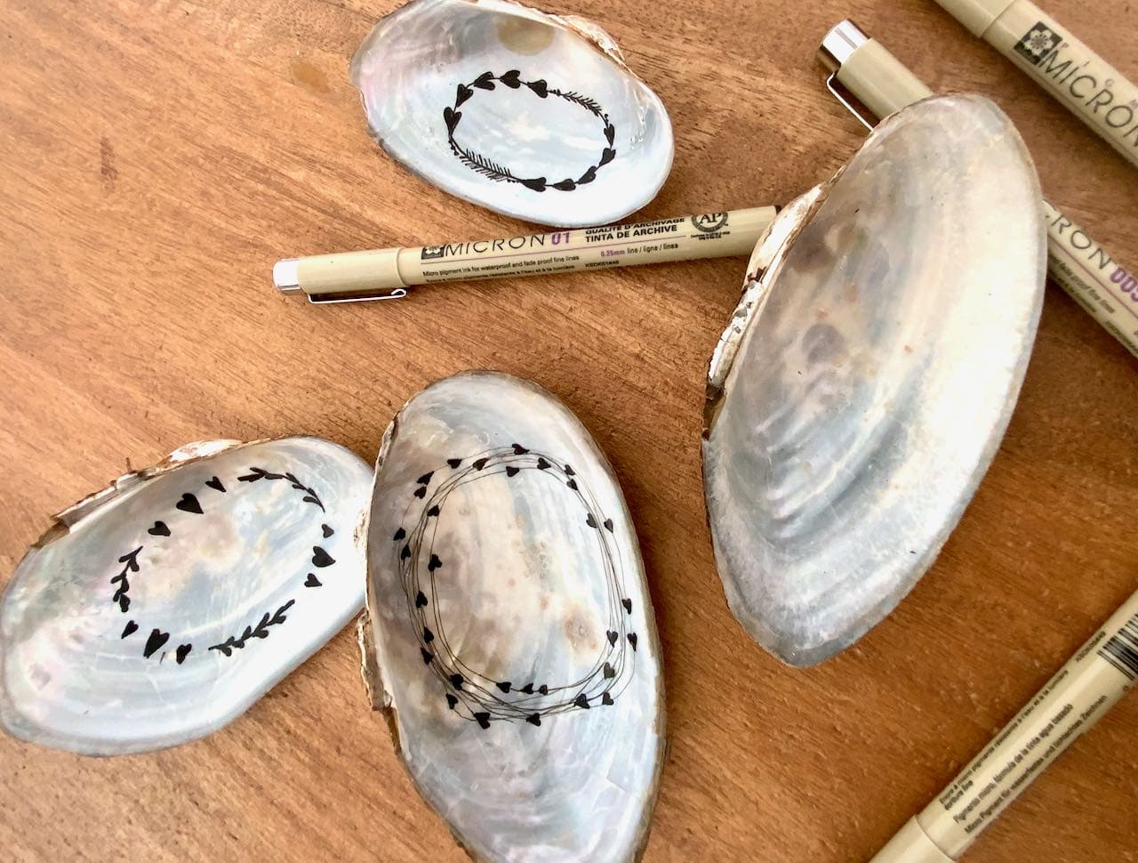 micron pens with doodled hearts inside shells on wood table