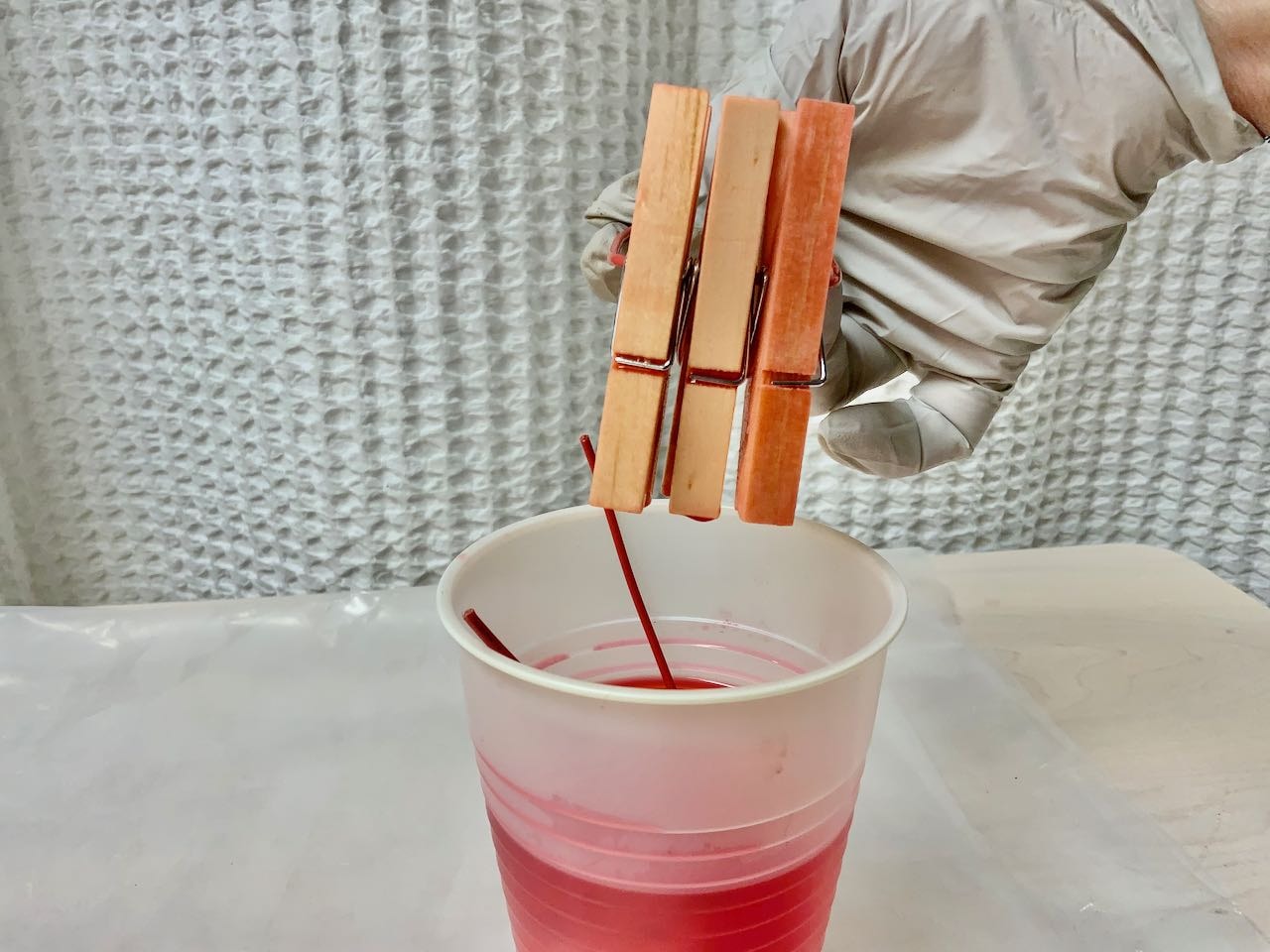 Gloved hand holding a set of three clothespins over the cup of dye, letting the dye drip off