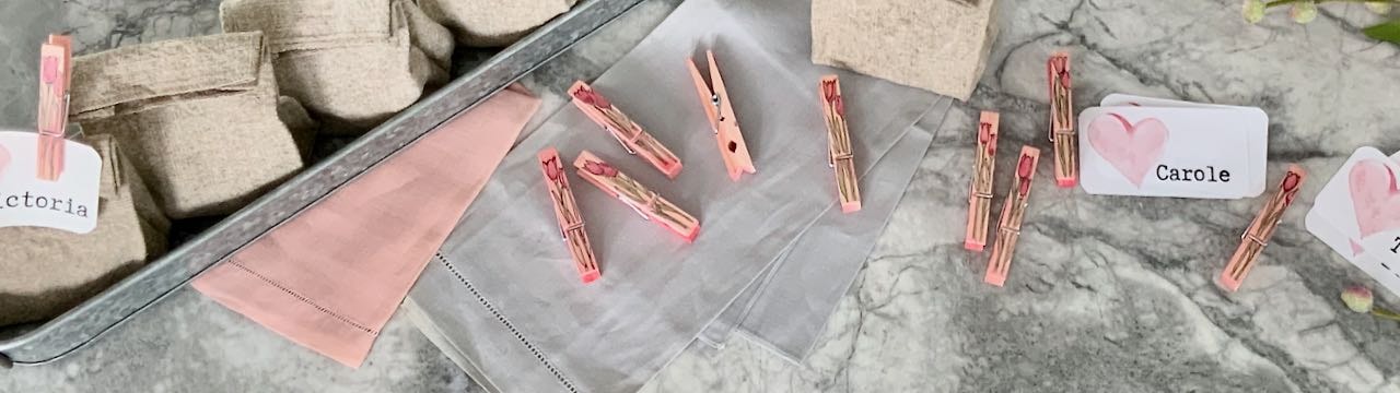 galvanized steel stary holding washed linen party favor bags on a quartz countertop with tulip decorated clothespins and valentine name tags scattered about