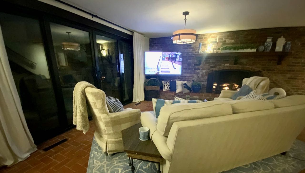 couch with swivel chair and fuzzy throw facing a tv with a sold wall of glass at night