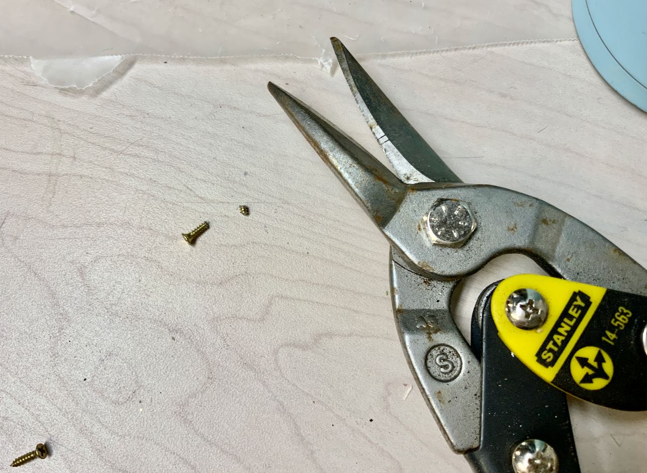 Metal Snips next to a screw head and just the tip of the screw cut off