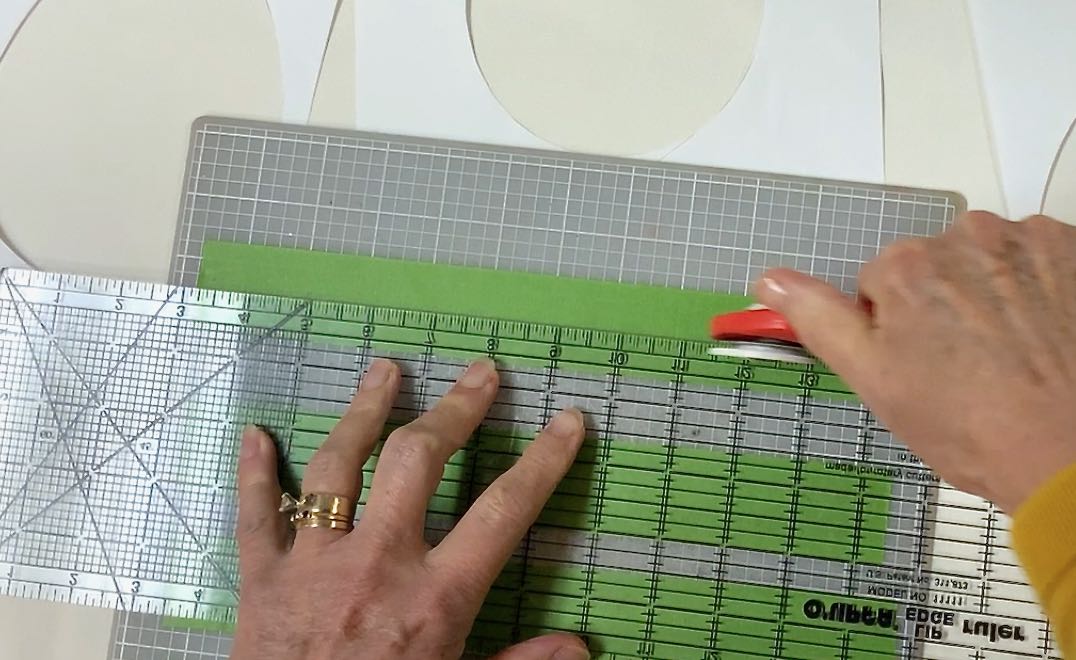 Hands holding a clear ruler on top of e painters and cutting with a rotary cutter 