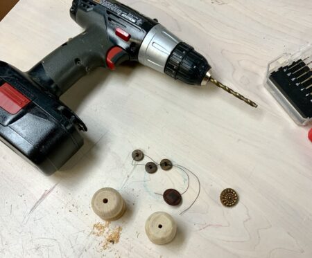 Drill with two wooden candle cups and a few buttons on the work table