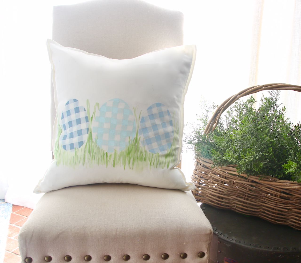 Finished plaid Egg Pillow on linen parsons chair with a drum case side table and large basket of green foilage