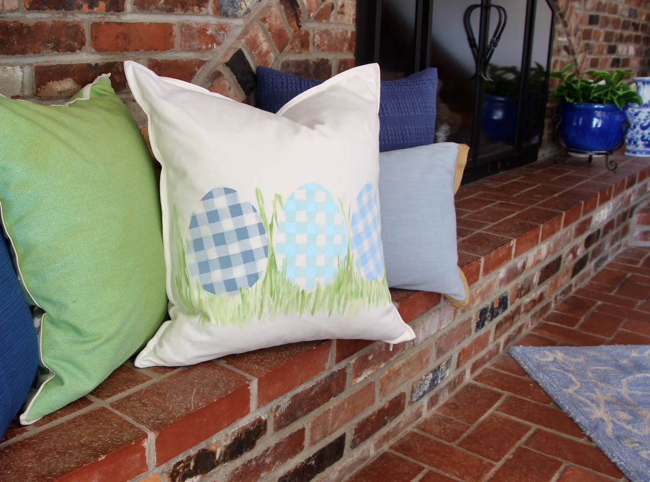 angle view of plaid eggs pillow with other solid pillows on a brick wall hearth