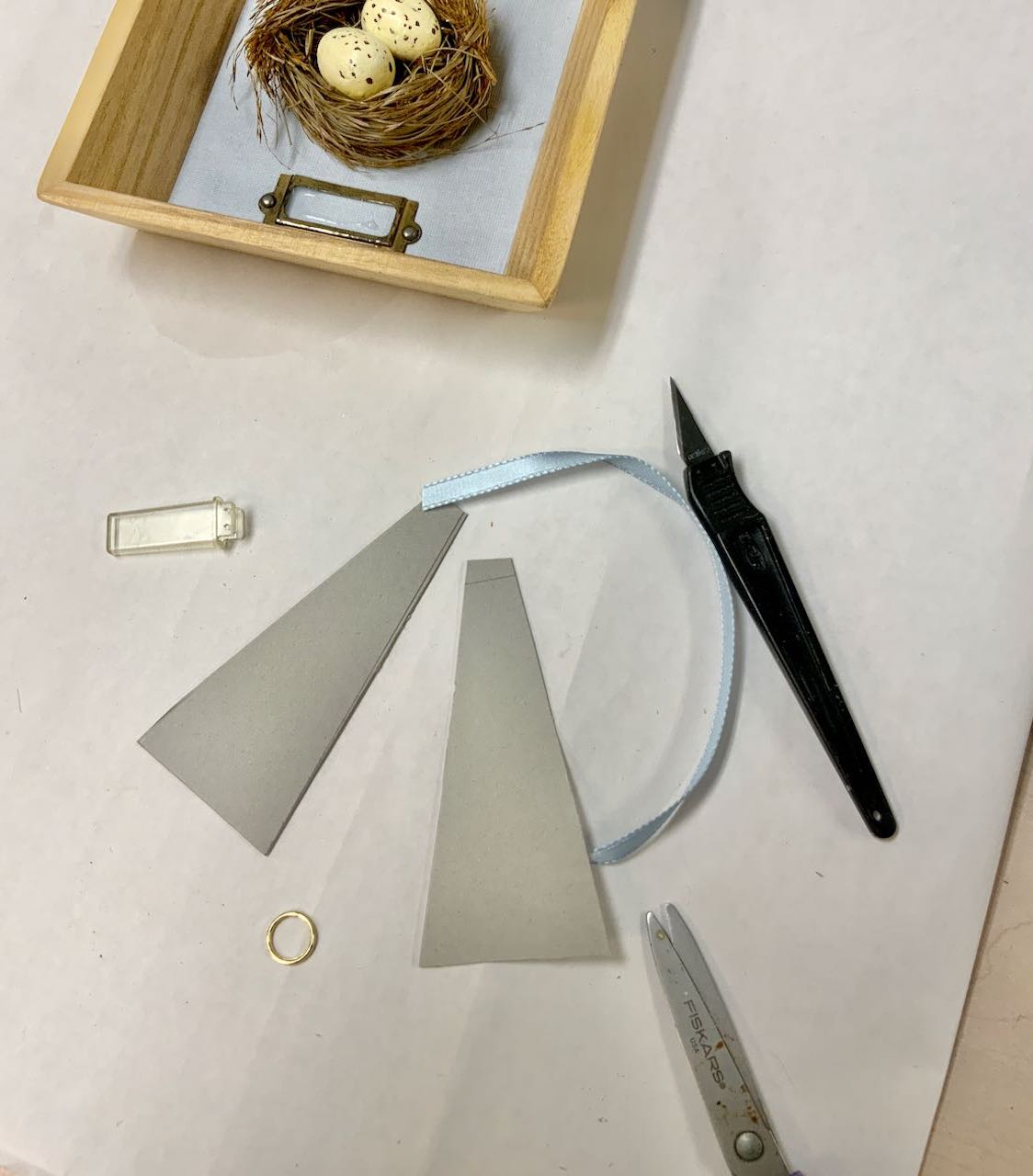 two triangles cut of cardboard with exacto knife, ribbon and small metal ring