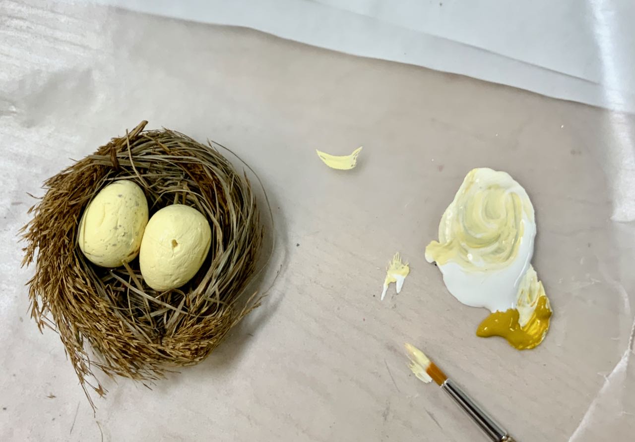 freshly painted eggs in nest with paintbrush and paint nearby