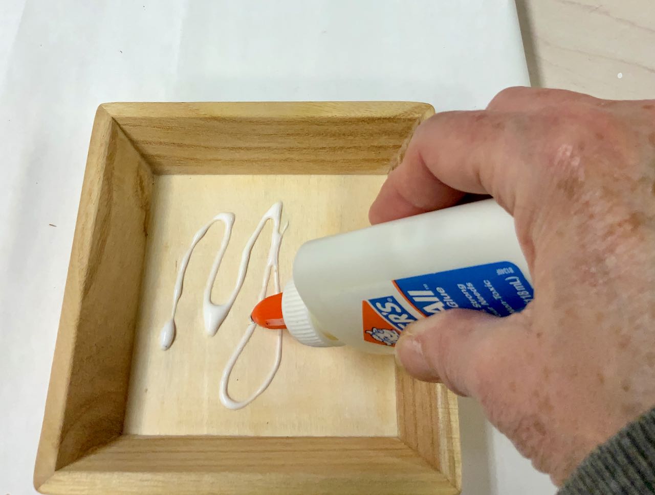 hand squirting elmers glue into wood box