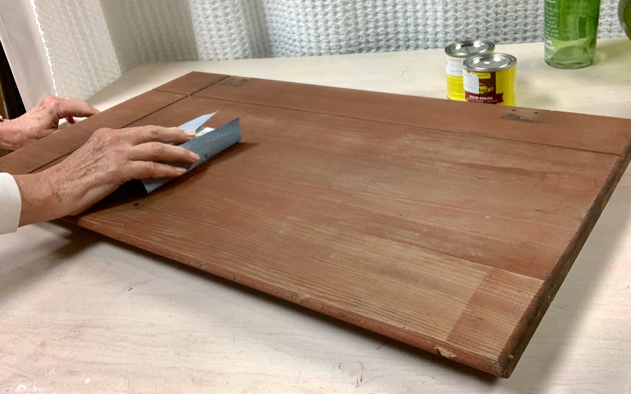 a hand holding a high grit sandpaper on a sanding block lightly sanding the cabinet door fronts