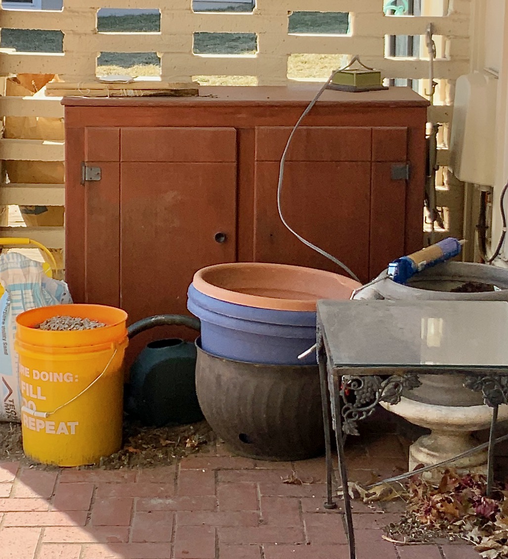 poor neglected old wood cabinet sitting in the corner of the patio with "stuff" piled around it